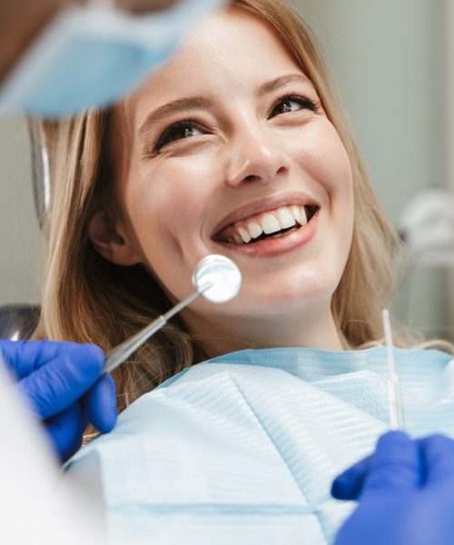 Image of pretty young woman sitting in dental chair at medical center while professional doctor fixing her teeth